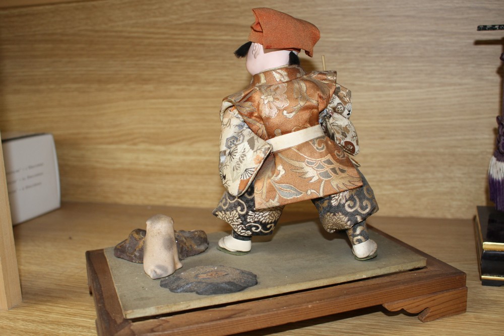 A Japanese late Meiji period composition and fabric figure of a boy farmer holding an adze with puppy seated nearby, mounted on display